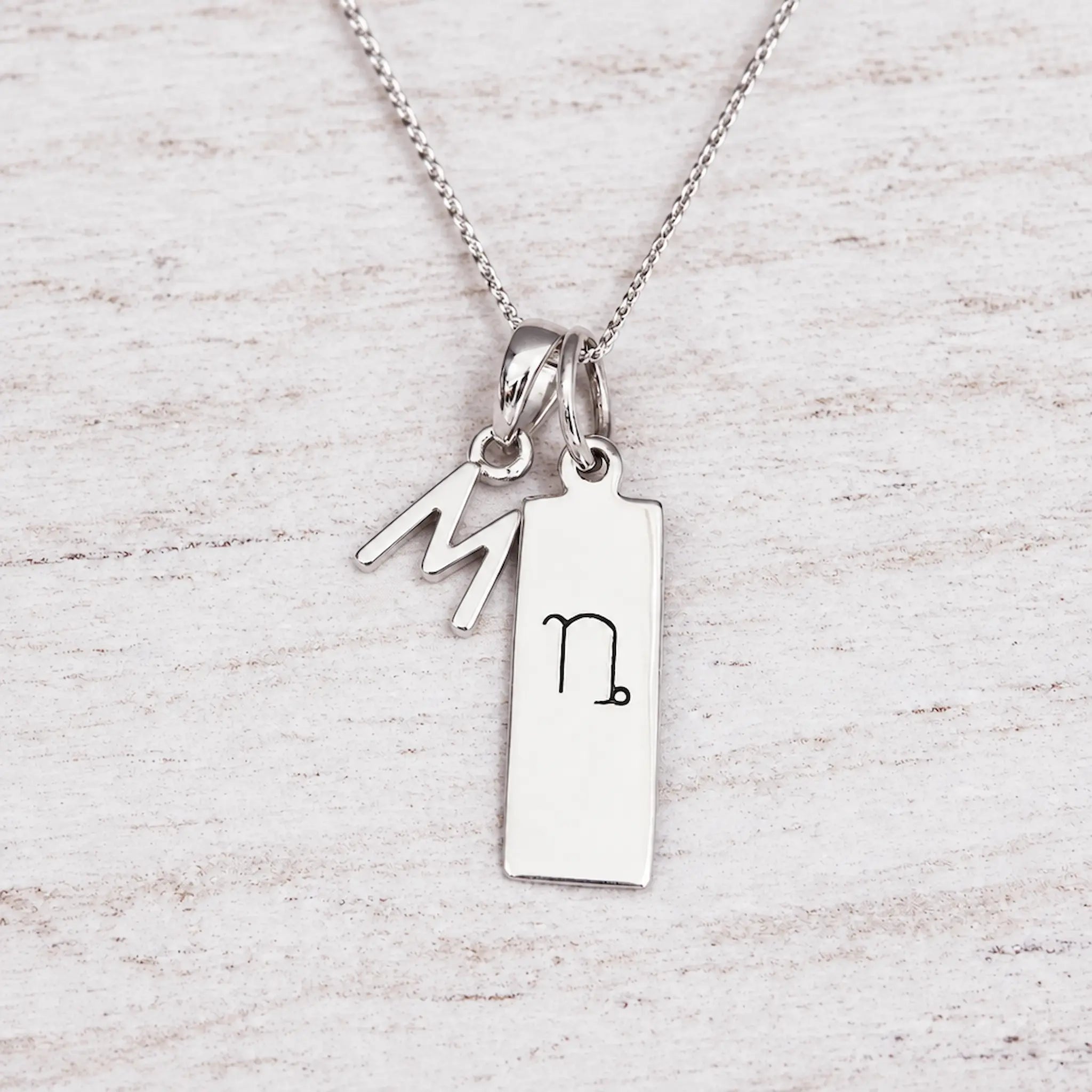 Silver Initial and Capricorn Zodiac Necklace with sterling silver letter M pendant on light wood