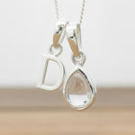 Silver Initial D necklace with a teardrop-shaped Herkimer Quartz crystal pendant hanging above a rustic wooden surface