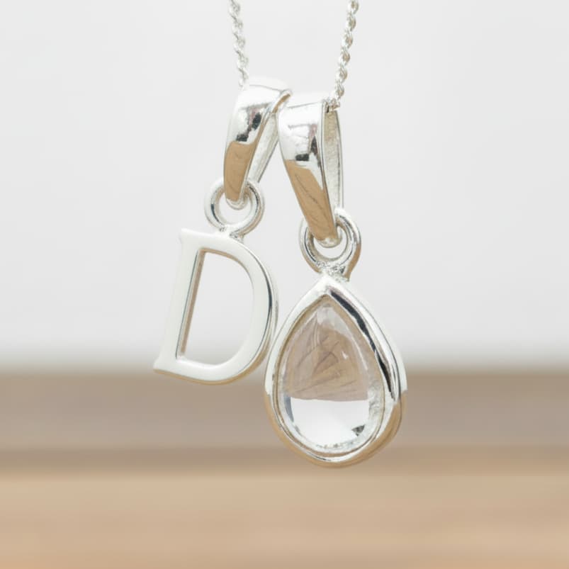 Silver Initial D necklace with a teardrop-shaped Herkimer Quartz crystal pendant hanging above a rustic wooden surface