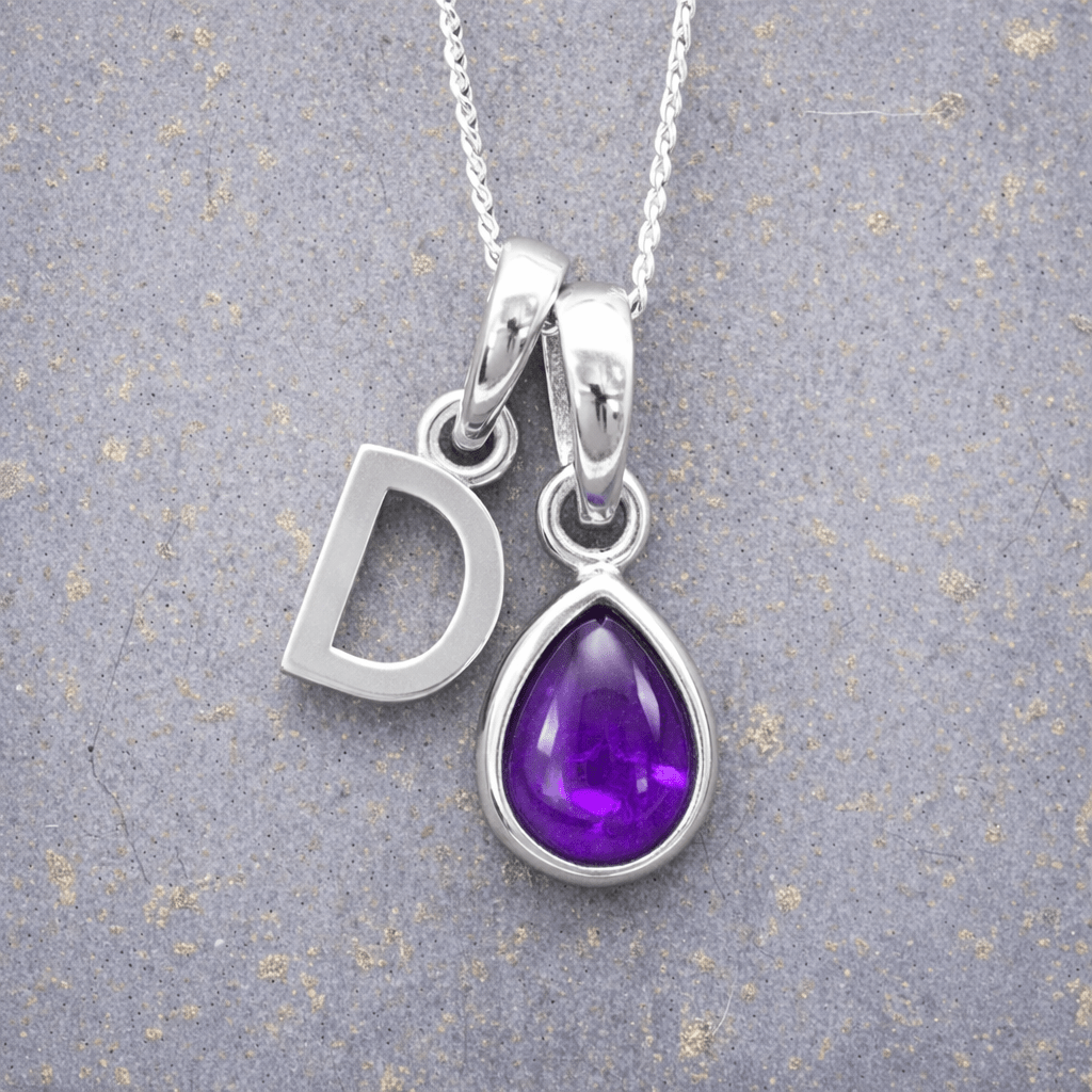 Silver necklace with 'D' initial pendant and purple teardrop february birthstone amethyst gemstone pendant on a textured grey background