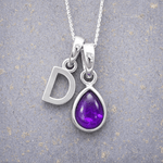 Silver necklace with 'D' initial pendant and purple teardrop february birthstone amethyst gemstone pendant on a textured grey background