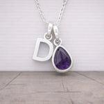 Silver necklace with 'D' pendant and purple amethyst teardrop gem on a light gray background