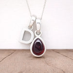 Silver Initial D necklace with a teardrop-shaped Garnet gemstone pendant hanging above a rustic wooden surface