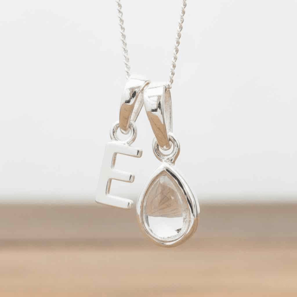 Silver Initial E necklace with a teardrop-shaped Herkimer Quartz crystal pendant hanging above a rustic wooden surface