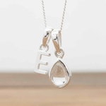 Silver Initial E necklace with a teardrop-shaped Herkimer Quartz crystal pendant hanging above a rustic wooden surface