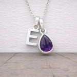 Silver necklace with 'E' pendant and purple amethyst teardrop gem on a light background