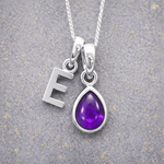 sterling Silver necklace with 'E' initial pendant and teardrop-shaped purple february birthstone amethyst gemstone on a textured grey background