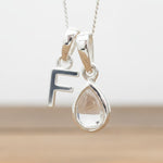 Silver Initial F necklace with a teardrop-shaped Herkimer Quartz crystal pendant hanging above a rustic wooden surface