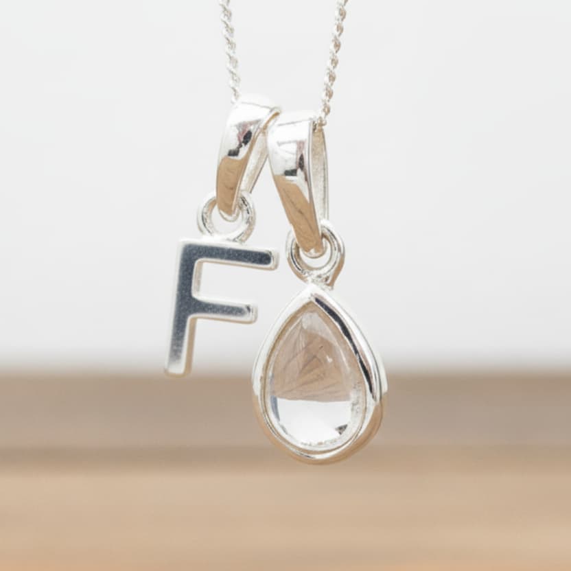 Silver Initial F necklace with a teardrop-shaped Herkimer Quartz crystal pendant hanging above a rustic wooden surface
