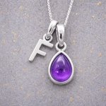 sterling Silver necklace with a purple teardrop february birthstone amethyst pendant and letter 'F' charm on a textured grey background.