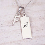 Sterling silver initial F and Sagittarius zodiac bar necklace, close-up of the letter charm and pendant on whitewashed wood