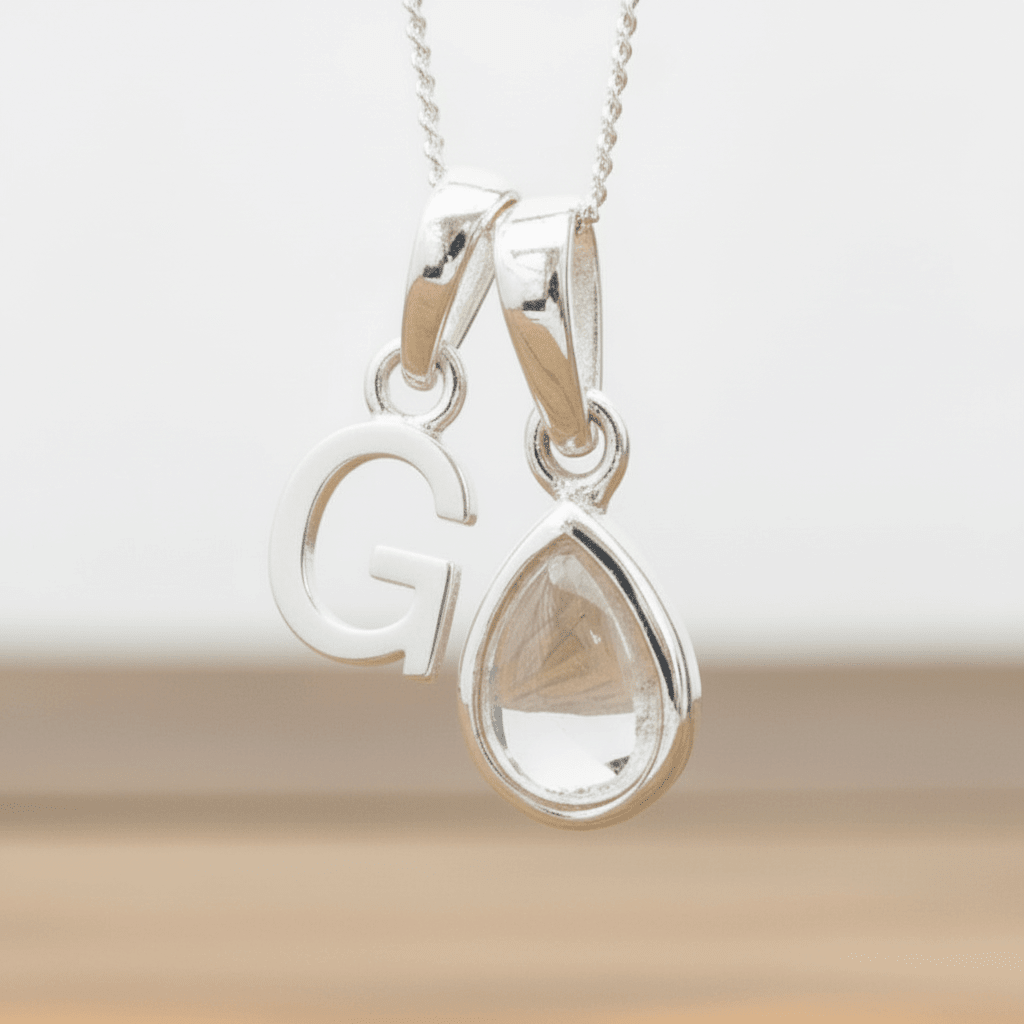 Silver Initial G necklace with a teardrop-shaped Herkimer Quartz crystal pendant hanging above a rustic wooden surface