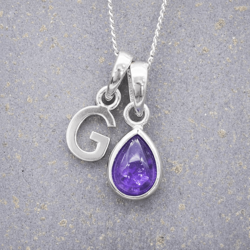 sterling Silver necklace with a 'G' initial pendant and a teardrop-shaped purple february birthstone amethyst gemstone on a grey background.