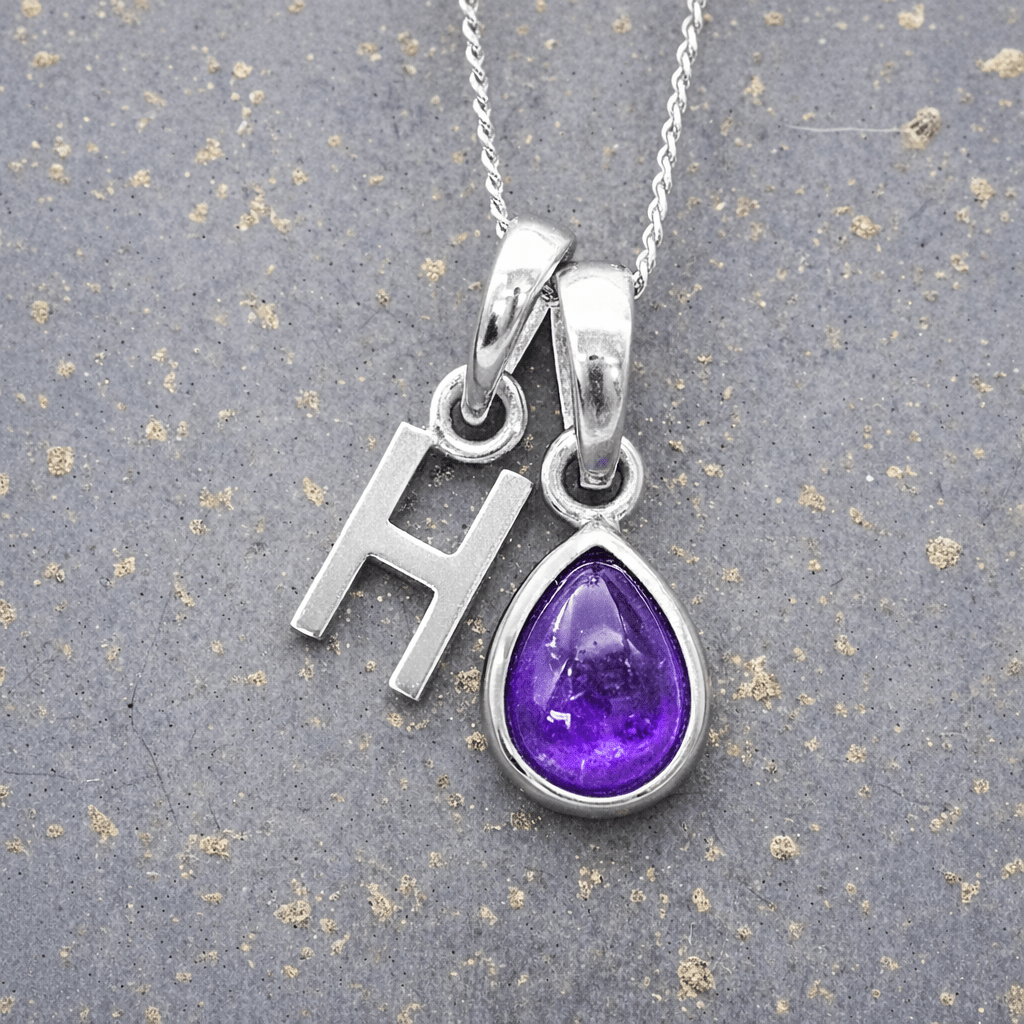 sterling Silver necklace with 'H' initial pendant and purple teardrop february birthstone amethyst pendant on a textured grey background