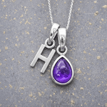 sterling Silver necklace with 'H' initial pendant and purple teardrop february birthstone amethyst pendant on a textured grey background