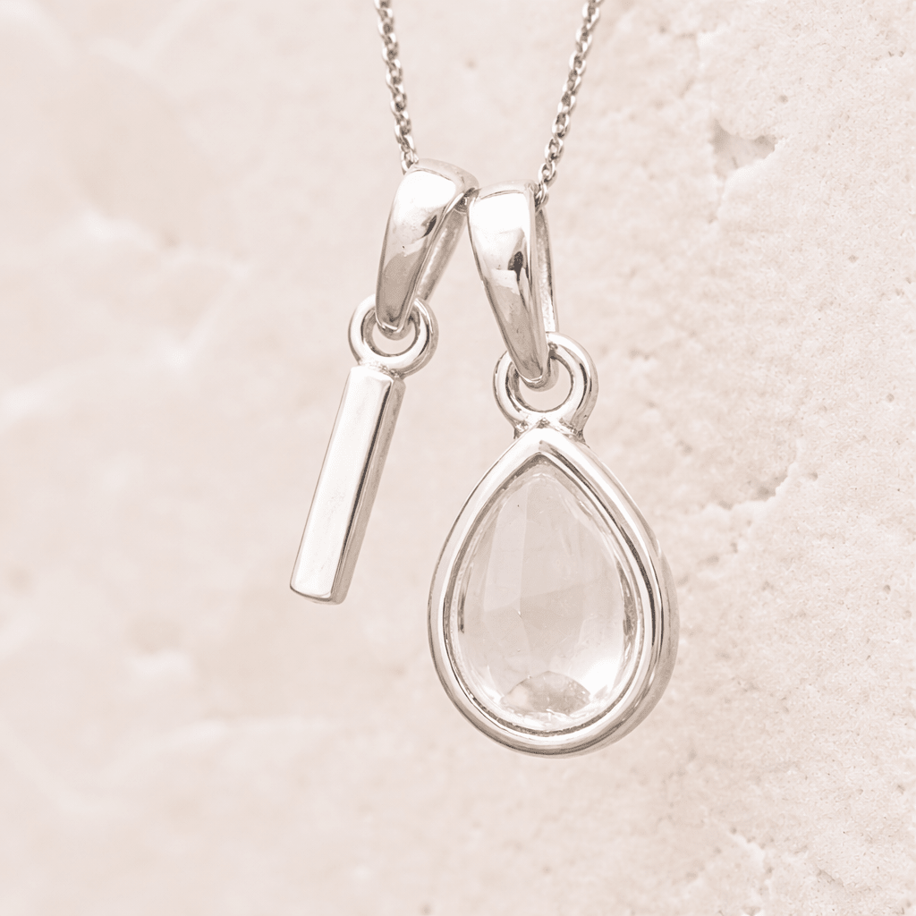 sterling Silver necklace with a 'I' initial pendant and pear shaped herkimer quartz pendant on a light beige background