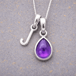 sterling Silver necklace with a 'J' initial pendant and purple teardrop february birthstone amethyst pendant on a textured grey background
