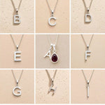 Collection of silver letter pendants a, b, c, d, e, f, g, h, i on a beige background as personalised initial options for a January Birthstone Natural Garnet Gemstone Necklace.