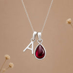 Sterling silver january birthstone garnet necklace with polished uppercase A initial charm on a beige stone 