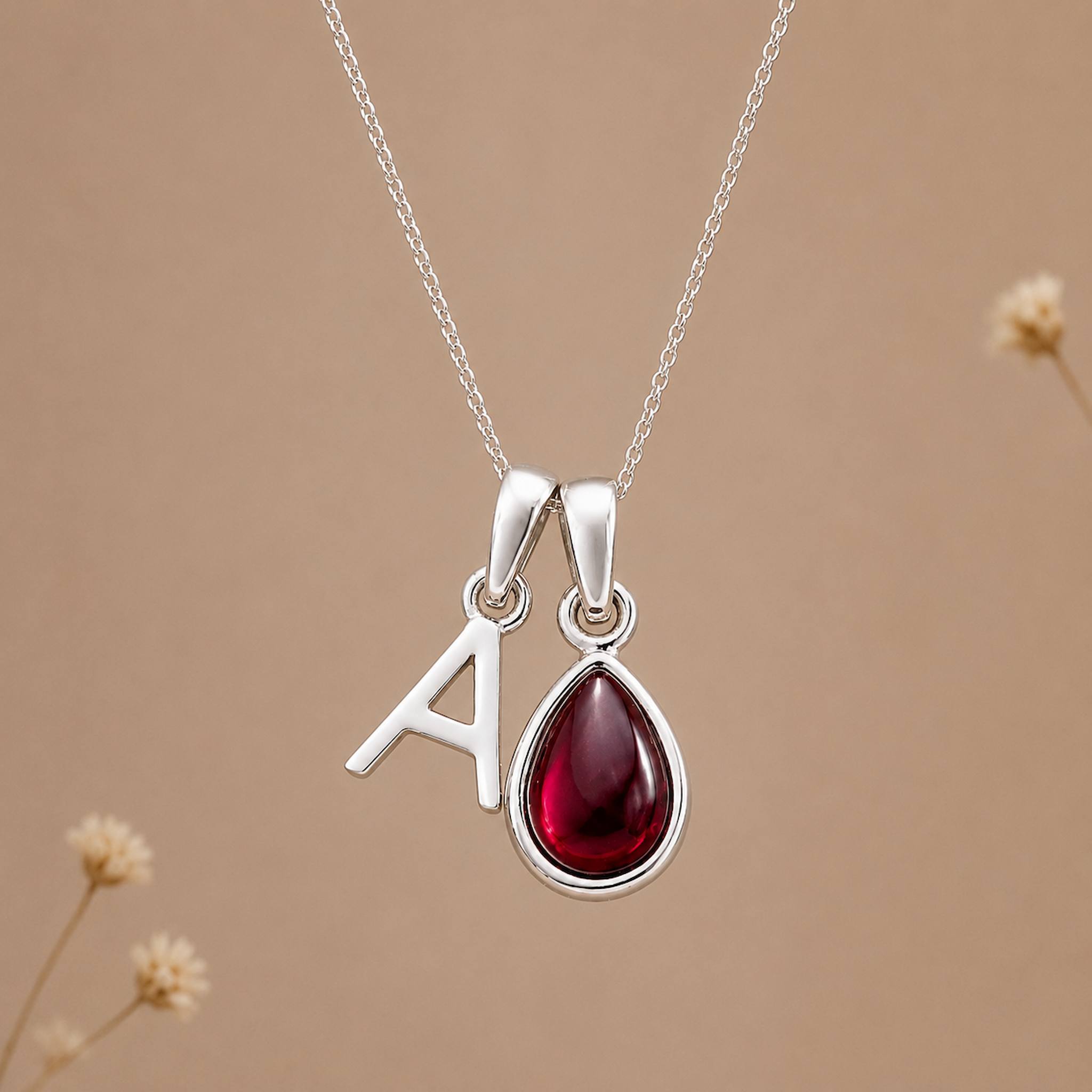 Sterling silver january birthstone garnet necklace with polished uppercase A initial charm on a beige stone 