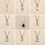 Collection of silver letter pendants a, j, k, l, m, n, o, p, q on a beige background as personalised initial options for a January Birthstone Natural Garnet Gemstone Necklace.