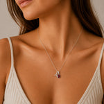 A close-up of a woman wearing a delicate silver necklace with two pendants - an A initial pendant and a teardrop-shaped natural garnet gemstone 