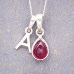 sterling silver initial a pendant and july birthstone ruby necklace on a grey background
