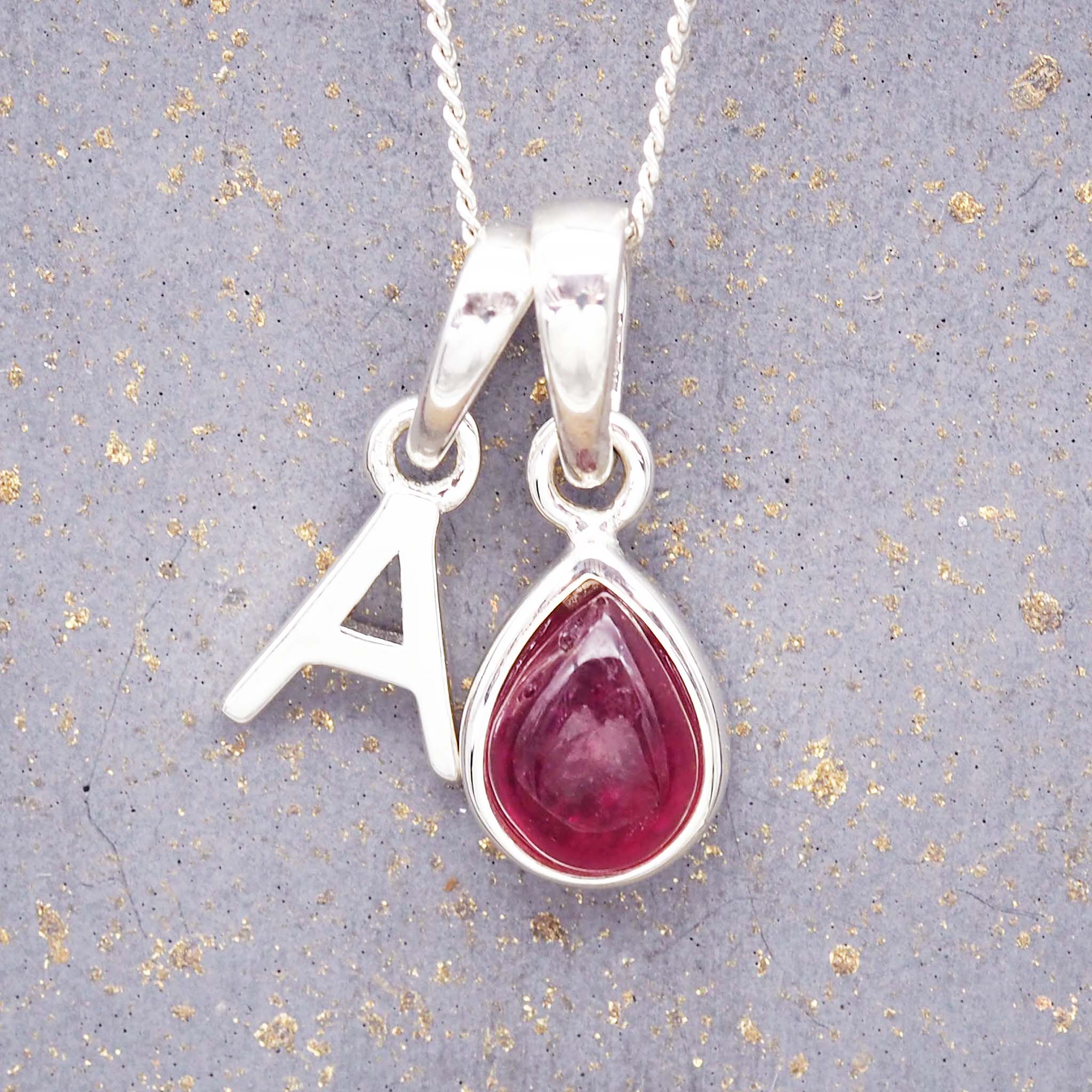 sterling silver initial a pendant and july birthstone ruby necklace on a grey background