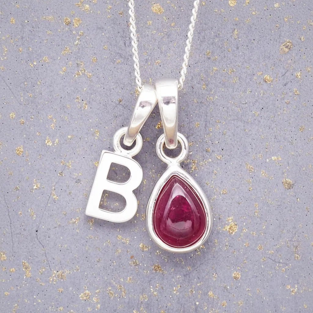 Sterling Silver necklace with 'B' initial pendant and July Birthstone Ruby gemstone pear-shaped pendant on a grey background.