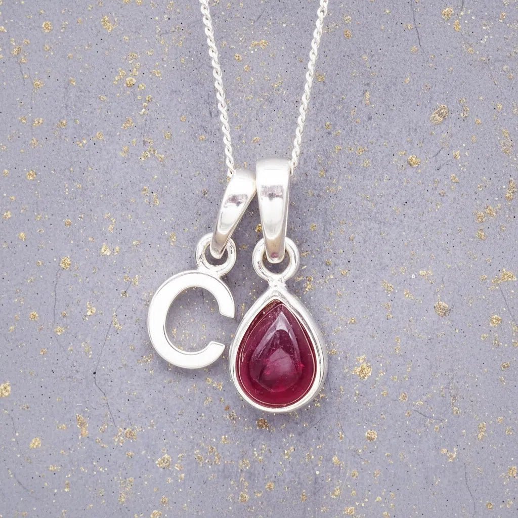 Sterling Silver necklace with 'C' initial pendant and July Birthstone Ruby gemstone pear-shaped pendant on a grey background.