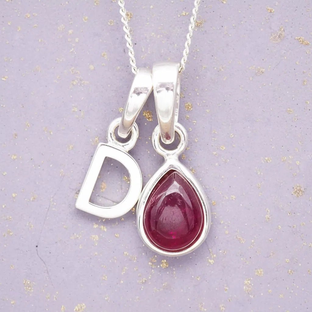 Sterling Silver necklace with 'D' initial pendant and July Birthstone Ruby gemstone pear-shaped pendant on a grey background.
