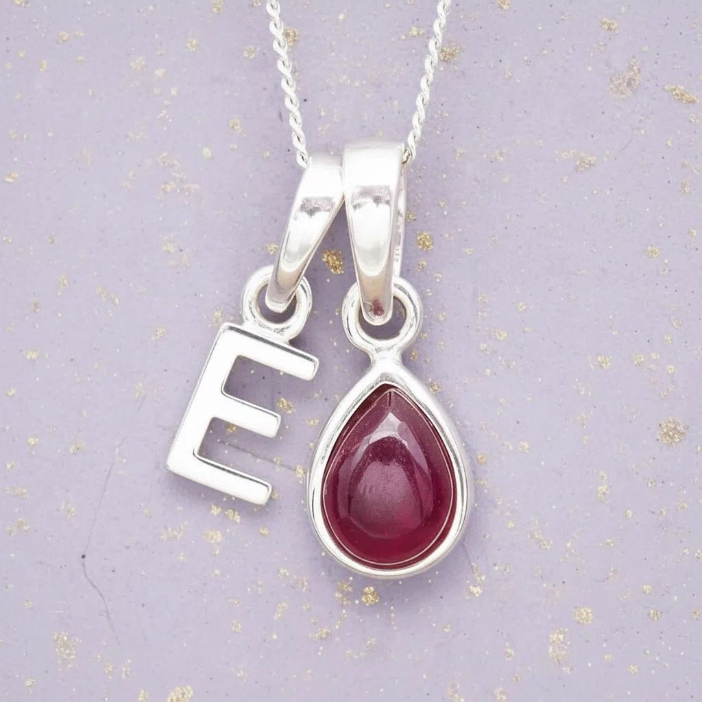 Sterling Silver necklace with 'E' initial pendant and July Birthstone Ruby gemstone pear-shaped pendant on a grey background.