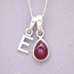 Sterling Silver necklace with 'E' initial pendant and July Birthstone Ruby gemstone pear-shaped pendant on a grey background.