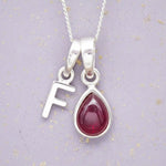 Sterling Silver necklace with 'F' initial pendant and July Birthstone Ruby gemstone pear-shaped pendant on a grey background.