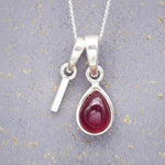 Sterling Silver necklace with 'I' initial pendant and July Birthstone Ruby gemstone pear-shaped pendant on a grey background.