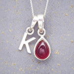 Sterling Silver necklace with 'K' initial pendant and July Birthstone Ruby gemstone pear-shaped pendant on a grey background.