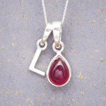 Sterling Silver necklace with 'L' initial pendant and July Birthstone Ruby gemstone pear-shaped pendant on a grey background.
