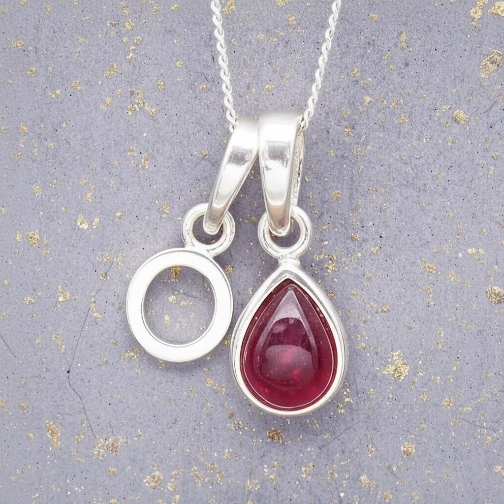 Sterling Silver necklace with 'O' initial pendant and July Birthstone Ruby gemstone pear-shaped pendant on a grey background.