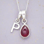 Sterling Silver necklace with 'P' initial pendant and July Birthstone Ruby gemstone pear-shaped pendant on a grey background.