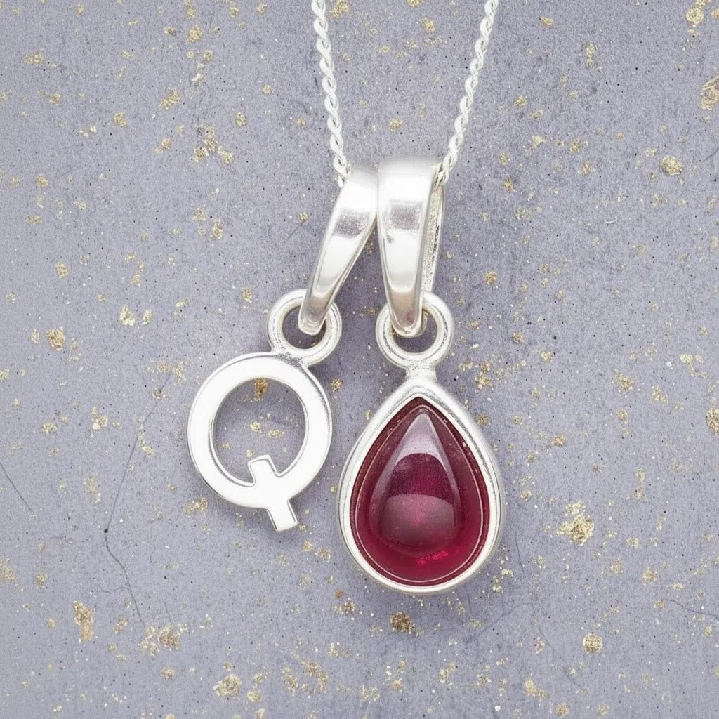 Sterling Silver necklace with 'Q' initial pendant and July Birthstone Ruby gemstone pear-shaped pendant on a grey background.