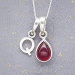 Sterling Silver necklace with 'Q' initial pendant and July Birthstone Ruby gemstone pear-shaped pendant on a grey background.