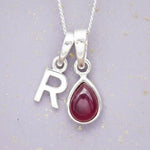 Sterling Silver necklace with 'R' initial pendant and July Birthstone Ruby gemstone pear-shaped pendant on a grey background.