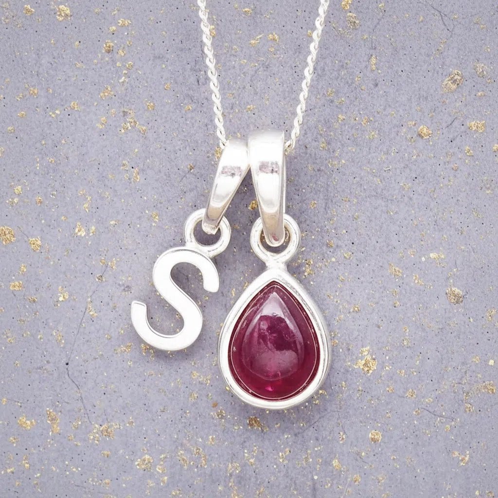 Sterling Silver necklace with 'S' initial pendant and July Birthstone Ruby gemstone pear-shaped pendant on a grey background.