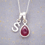 Sterling Silver necklace with 'S' initial pendant and July Birthstone Ruby gemstone pear-shaped pendant on a grey background.