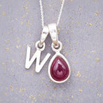 Sterling Silver necklace with 'W' initial pendant and July Birthstone Ruby gemstone pear-shaped pendant on a grey background.