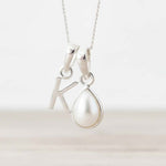 Silver necklace with 'K' initial pendant together with a pearl pendant on a white background