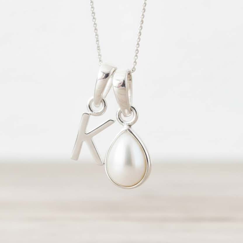 Silver necklace with 'K' initial pendant together with a pearl pendant on a white background