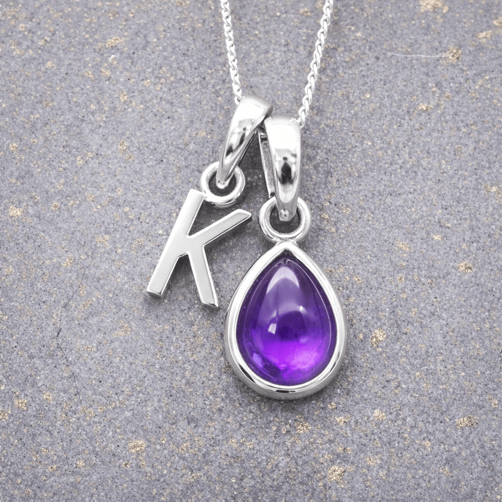 sterling Silver necklace with a purple teardrop february birthstone amethyst pendant and letter 'K' charm on a grey background
