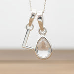 Silver Initial L necklace with a teardrop-shaped Herkimer Quartz crystal pendant hanging above a rustic wooden surface