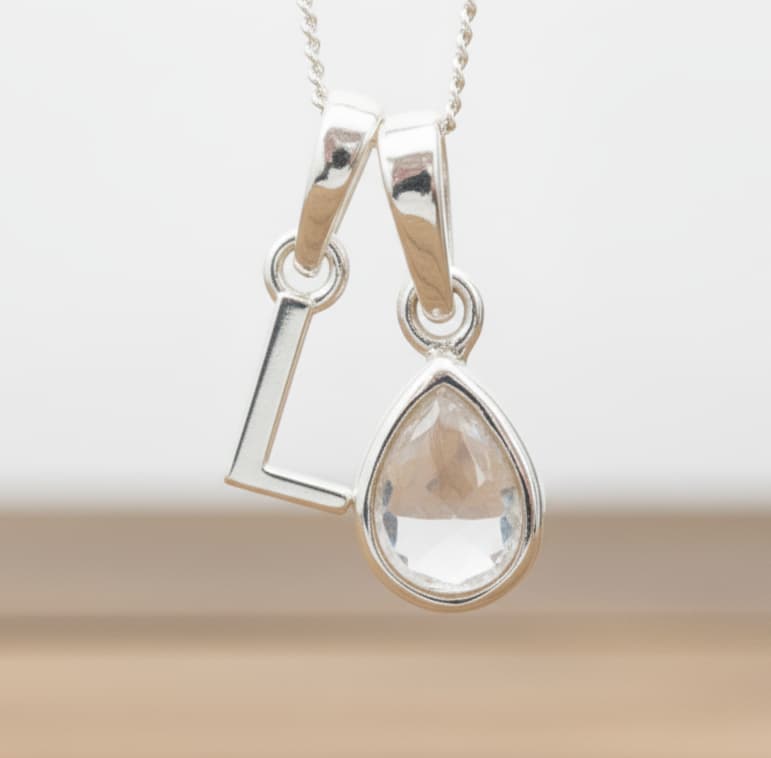 Silver Initial L necklace with a teardrop-shaped Herkimer Quartz crystal pendant hanging above a rustic wooden surface